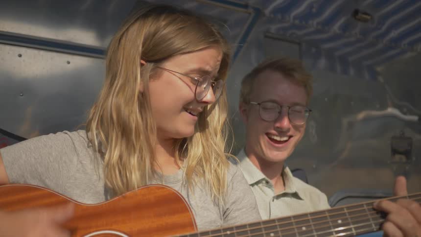 A white male and female that may be siblings are singing while the female playsguitar