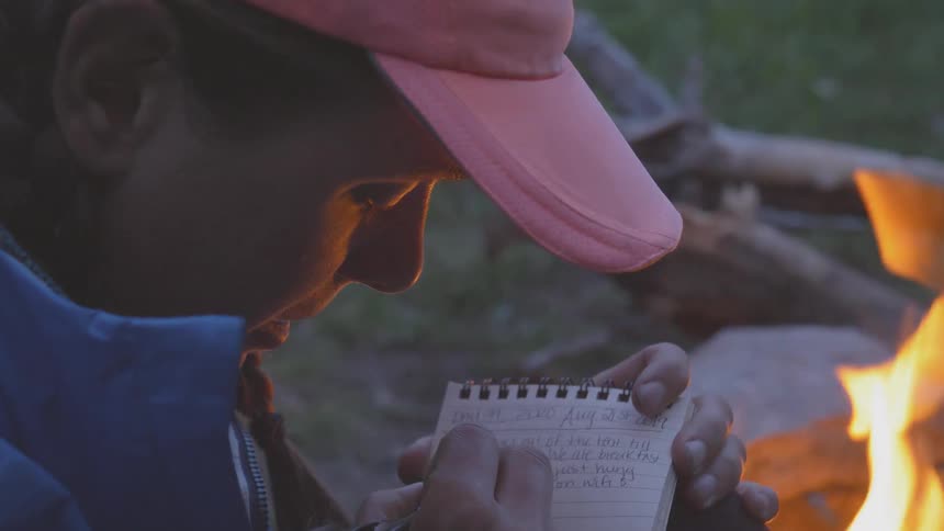 A girl writing on a paper in front of a bon fire