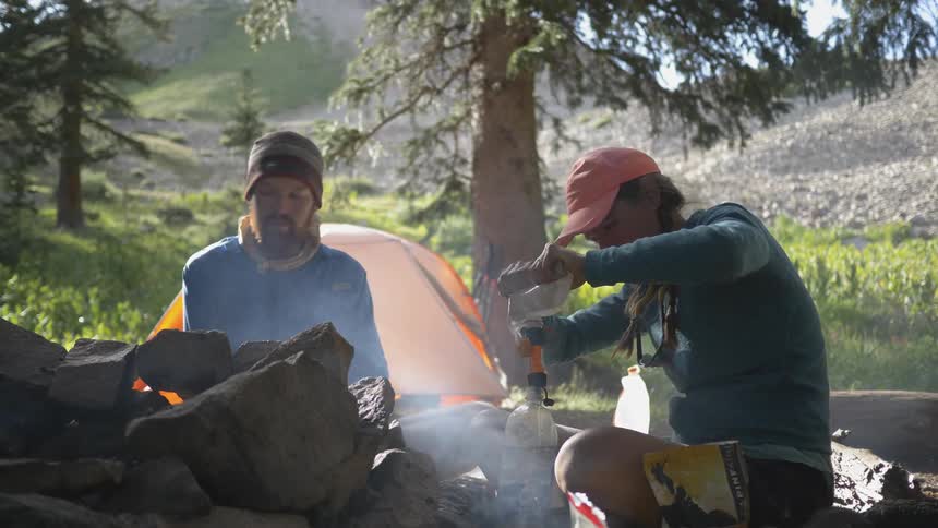 Campers sitting around a campfire refilling a water bottle