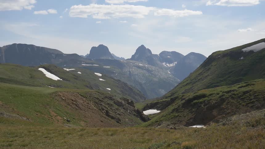 An expansive mountain range is covered in lush green vegetation and the occasional patch of snow