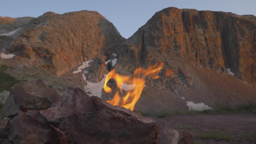A campfire burns near mountains
