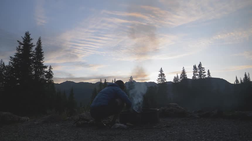 Man lights the campfire in the forest at dusk