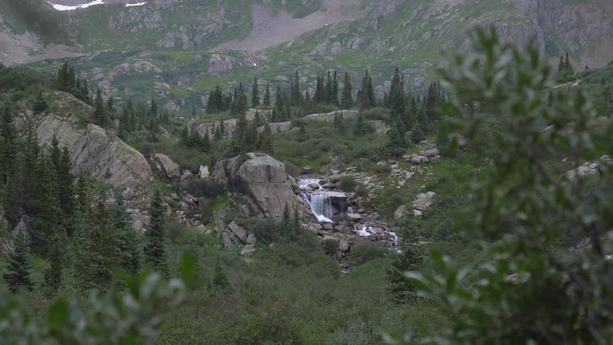 A waterfall can be seen from a distance within forested mountain range