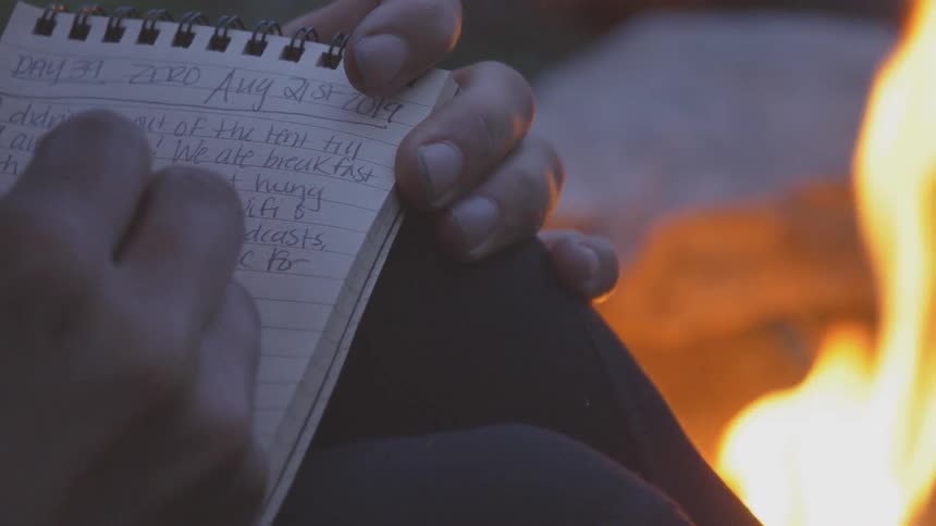 A person writing on a notebook by a fire