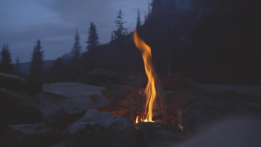 A campfire within a stone fire ring in the mountains at night