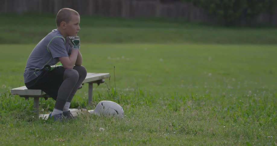 A boy waits on a bench in a field