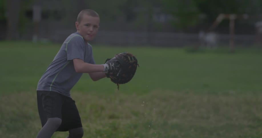 A boy scoops up and throws a baseball on a wet field