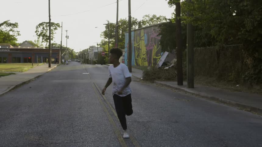 Black boy runs on the asphalt road in the neighbourhood