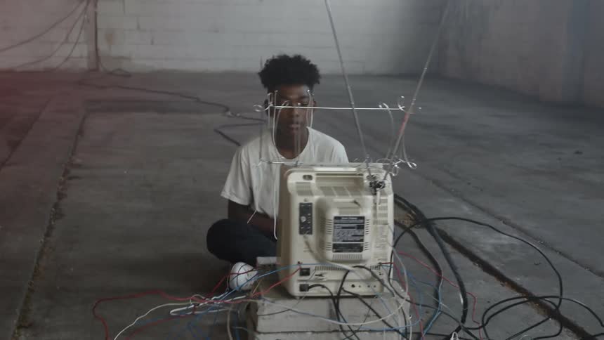 A teenager sits on the ground with electrodes running from his head to a television