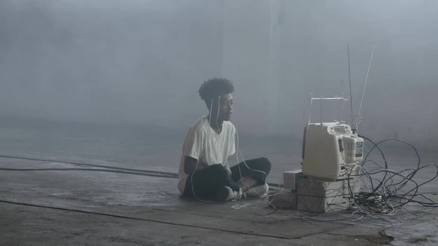 A boy sits on the floor with electrodes attached to his head leading to a computer