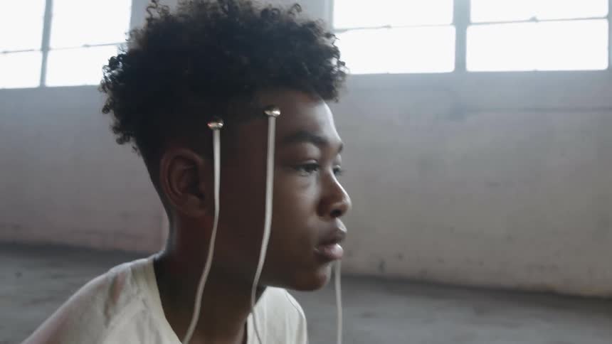 Boy sitting on concrete floor with two electrodes with wires are attached to each side of their head and his eyes dart up and down