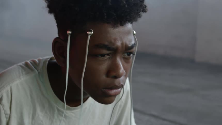 Black man with electrodes on his head sits and leans forward