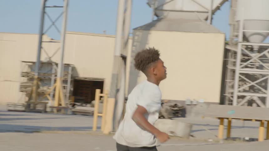 A boy look back as he runs through a factory lot on a sunny day