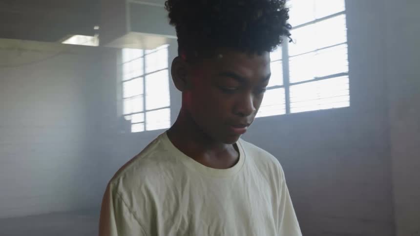 A boy stands in the center of a room looking down at a small television on the floor