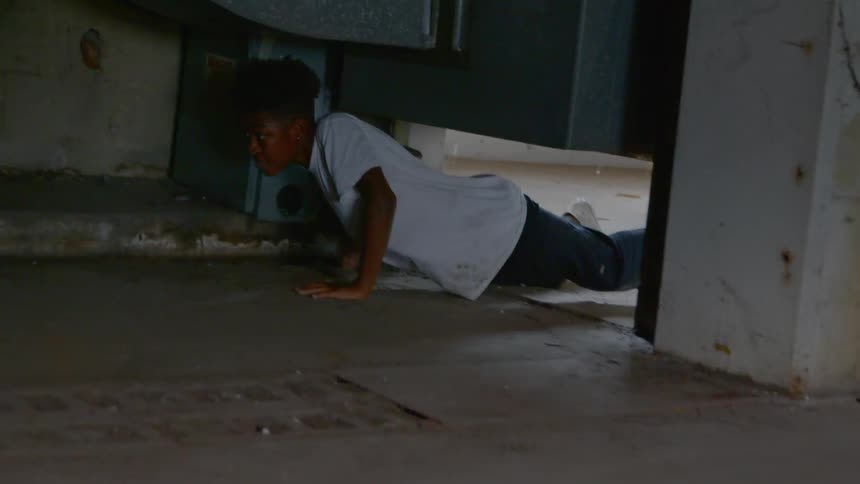 A boy crawls through an opening under a vent then runs away