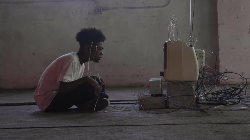 Young man with cables coming out of his head watches a vintage television