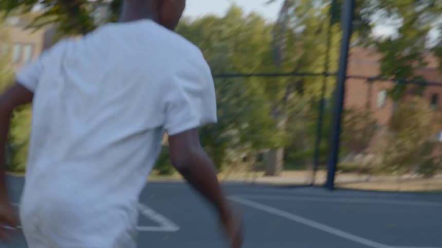 A boy runs through a basketball court and onto a sidewalk