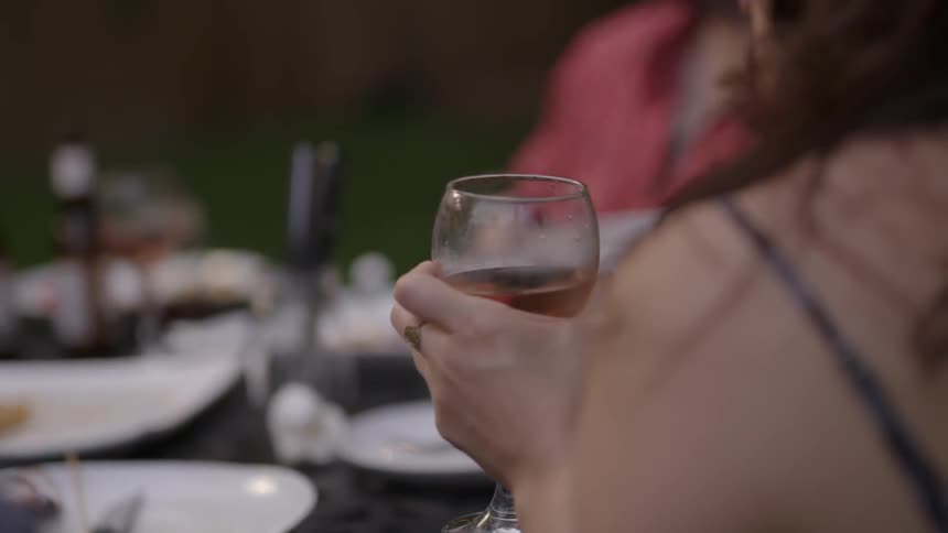 A woman holds a glass of wine as she sits with friends at a dinner table