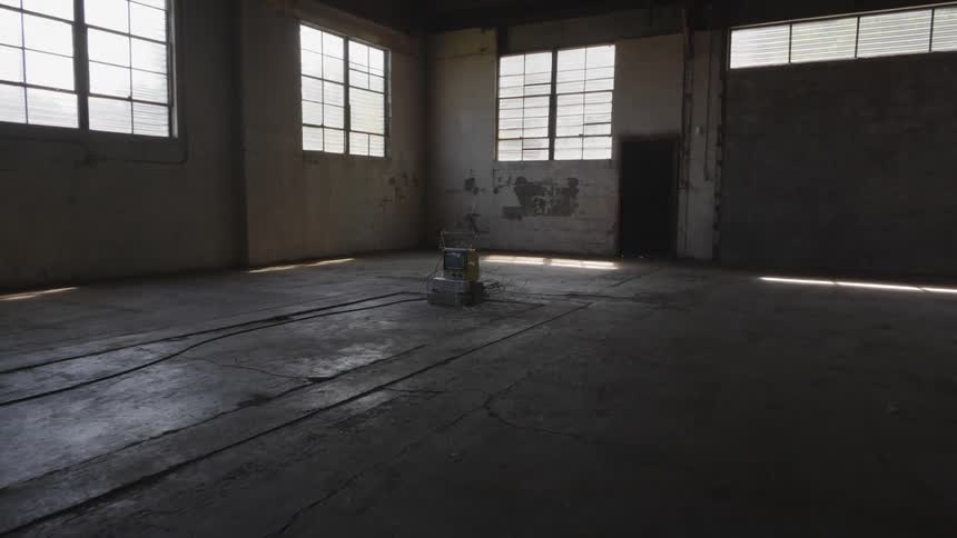 In an abandoned concrete garage an old fashioned television sits on the floor surrounded by a tangle of wires