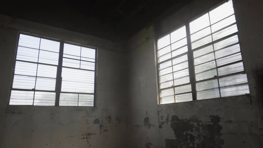 Paint peels off the walls near the windows of an empty room