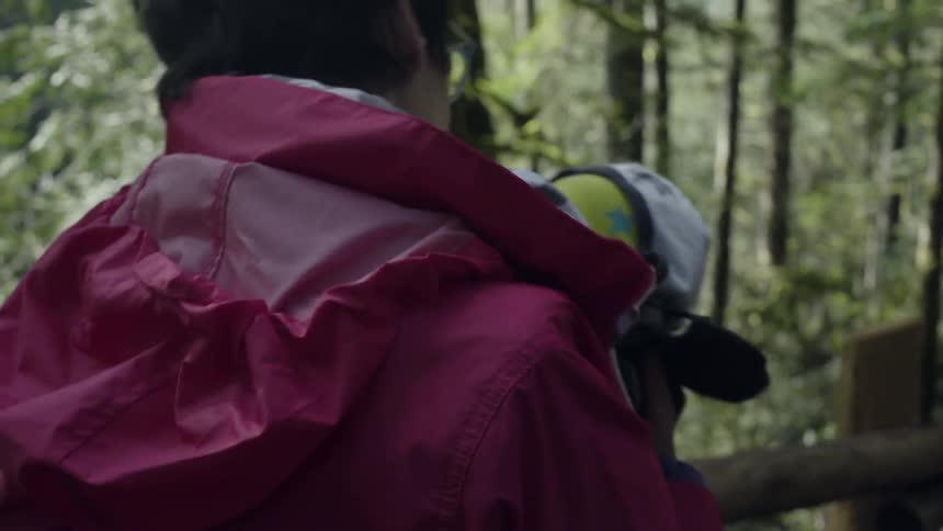A woman walks through the woods carrying a baby
