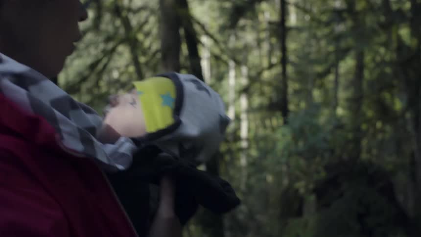 A woman carrying a baby is hiking through a forest