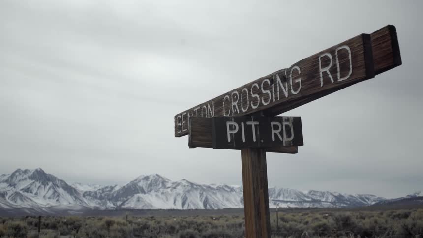 A wooden sign is posted with a mountain range in the background