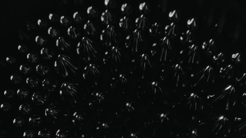 A closeup of the surface of a black ferromagnetic fluid shows the surface forms reflective spikes than then suddenly dissipate
