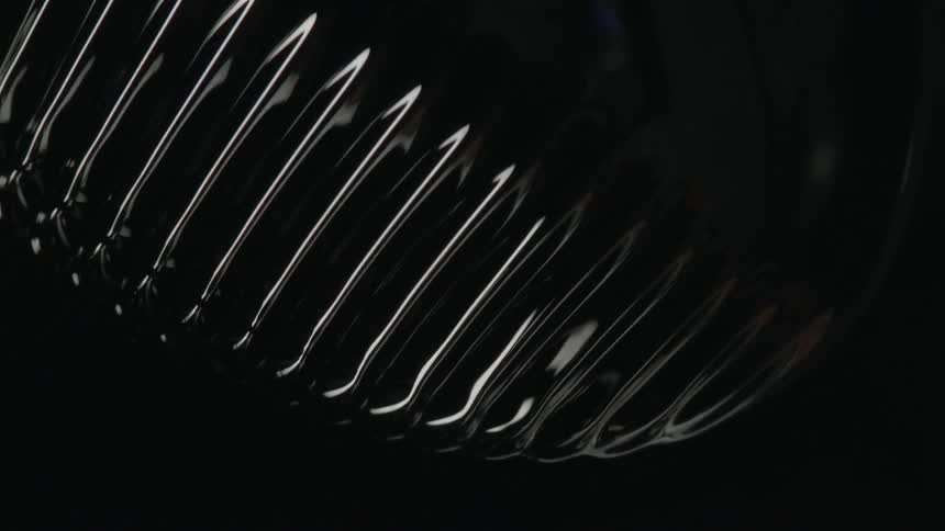 The surface of a shiny black ferromagnetic fluid is warped and distorted in a surreal manner