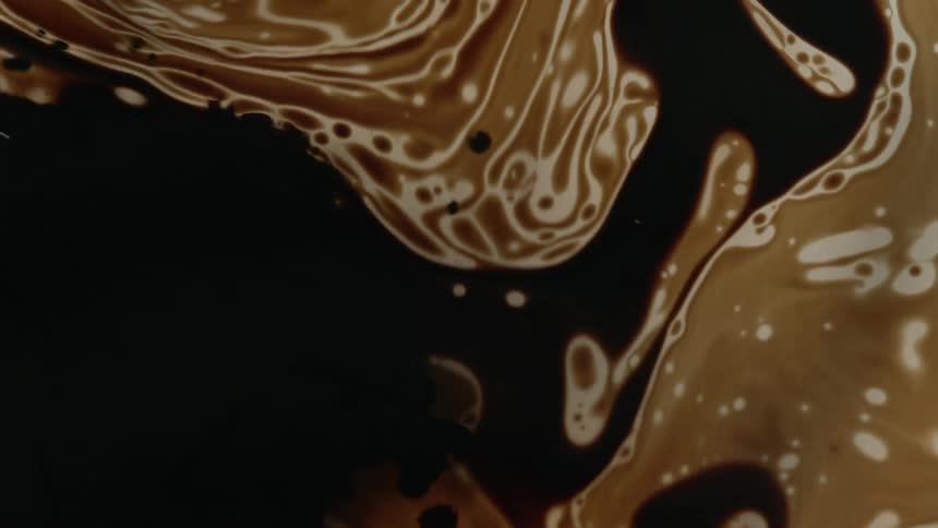 Dark liquid being poured in to a lighter brown liquid