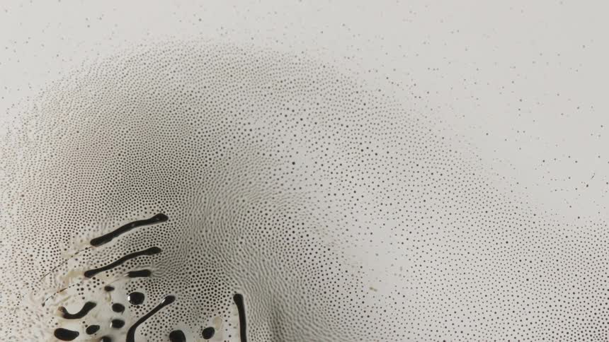 Amidst the white foamy swirl of a hundreds of tiny bubbles a handful of long dark liquid droplets move in an almost organic manner