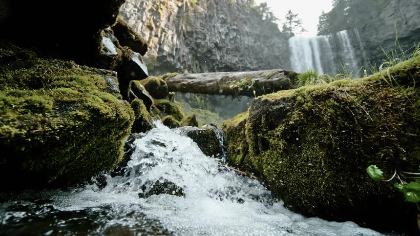 Water rushing over a small rock ledge with a larger waterfall upstream