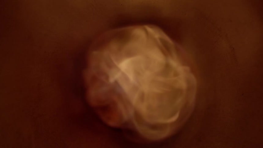 A darkened circular tube is illuminated as a small flame generates a swirl of smoke