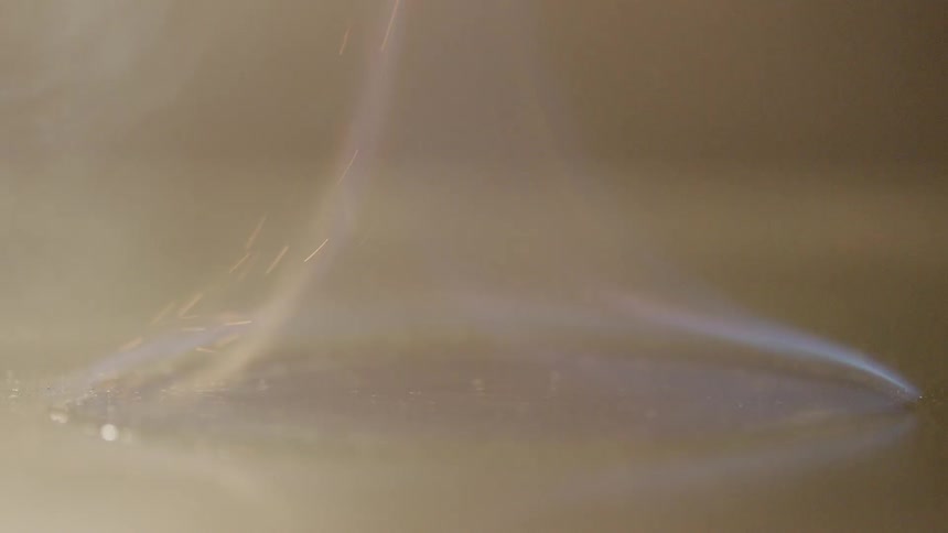A spark lights a fire atop a small spot of flammable fluid atop a shiny black surface