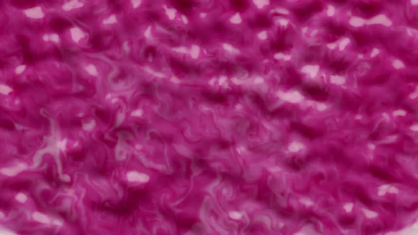 A magenta liquid begins to ripple and splash as it is vibrated strongly from beneath