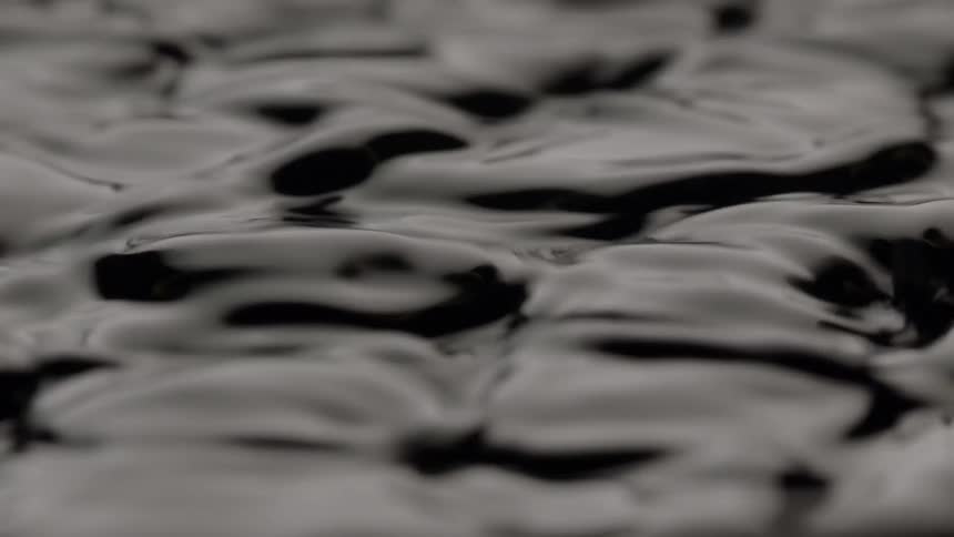 The surface of a shiny black liquid can be seen rippling very vigorously