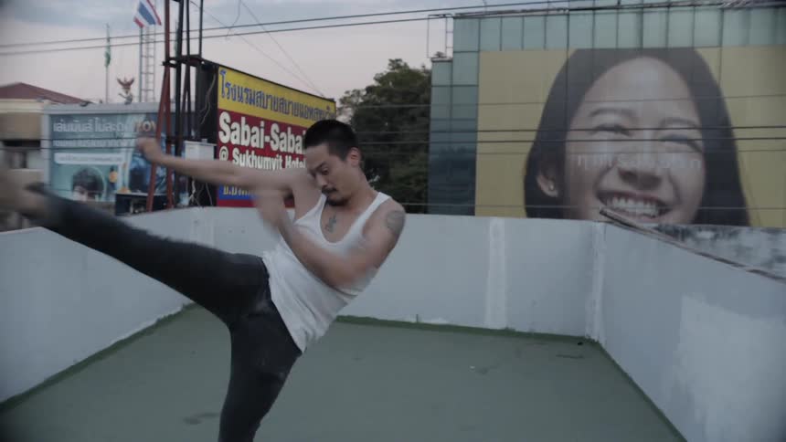 A man shadow boxes and kicks up on a city rooftop