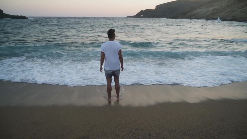 A man stands in the sandy coast line with ocean waves hitting his feet
