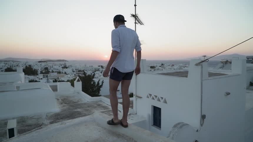 A man walks along the edge of a white roof at sunrise