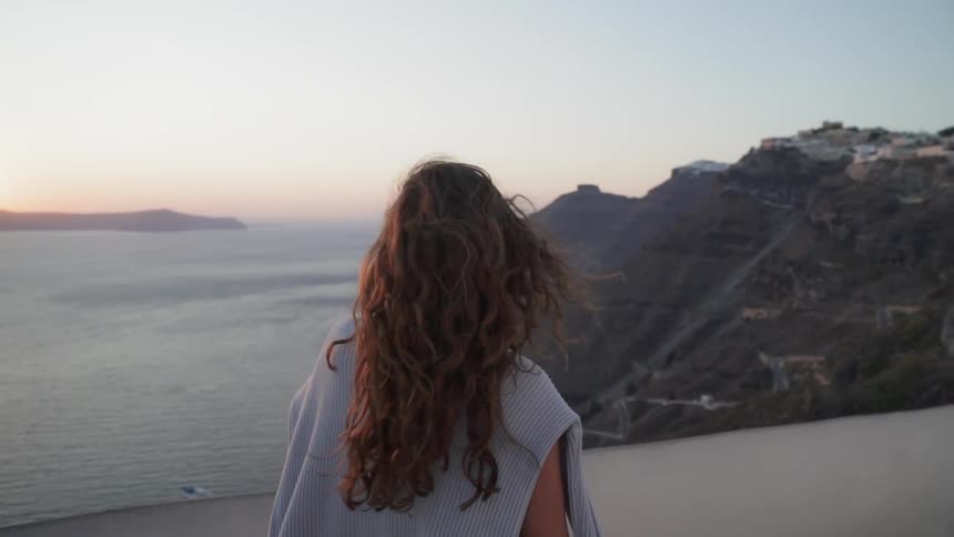 A woman walks on a rooftop overlooking the ocean at sunset