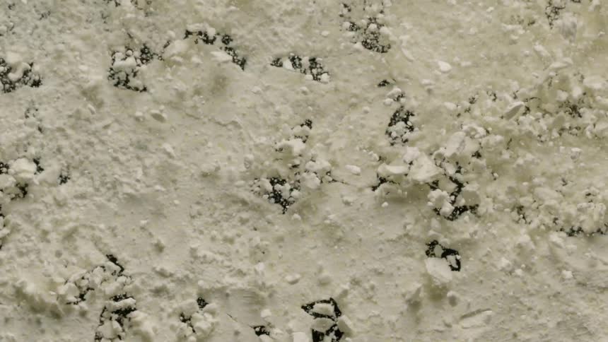 A cream colored surface is vibrating and begins to crumble and break apart