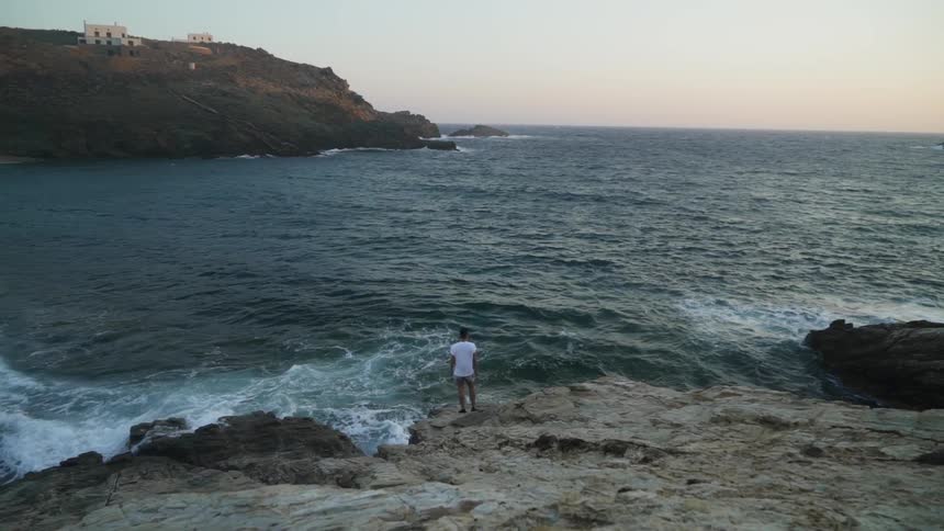 Man standing at edge of cliff in a cove watching waves crash on rocks