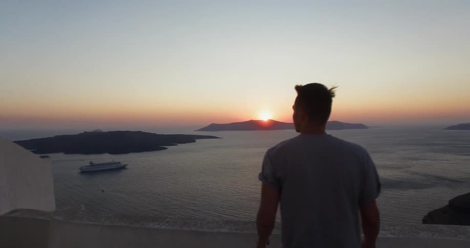 A man walks to a balcony and looks toward the ocean and coast