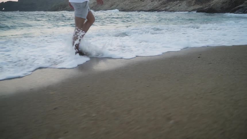 A man walks in the coastal sand as ocean waves come up and hits feet