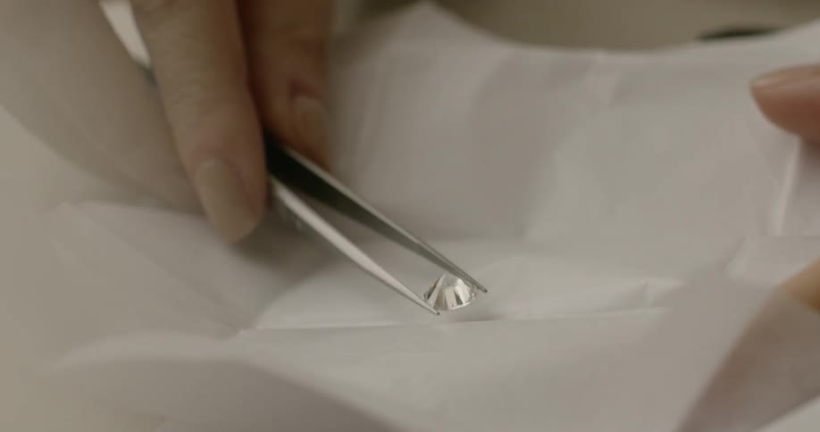 A hand picking up a diamond with tweezers from a white tissue paper