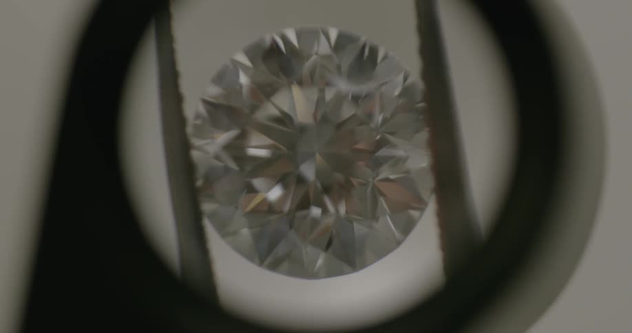 Someone inspects a diamond being held between tweezer tongs through a jewelers lens