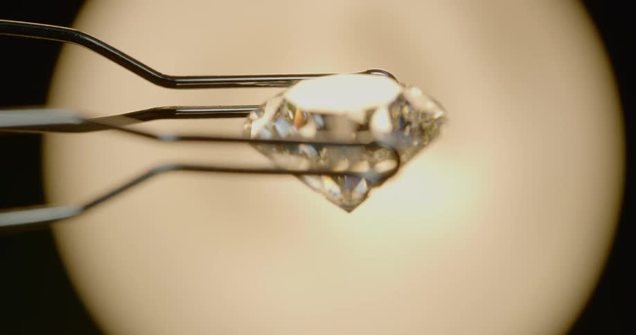 A diamond being held and rotated with a pair of tweezers before a light