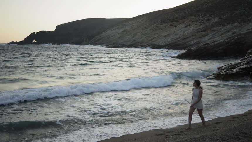 Woman walks barefoot along the beach at dusk
