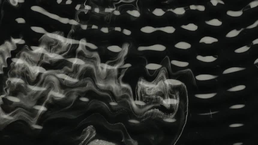 Wisp like patterns on a black liquid being disturbed as the liquid vibrates