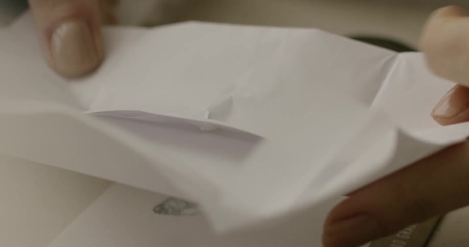 A person unfolds a folded piece of paper to find a gem stone